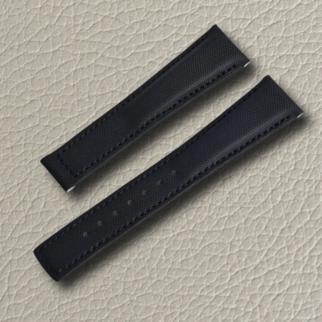 Onyx black sailcloth watch strap with textured surface, tonal stitching, and adjustment holes, displayed on a light beige leather background.
