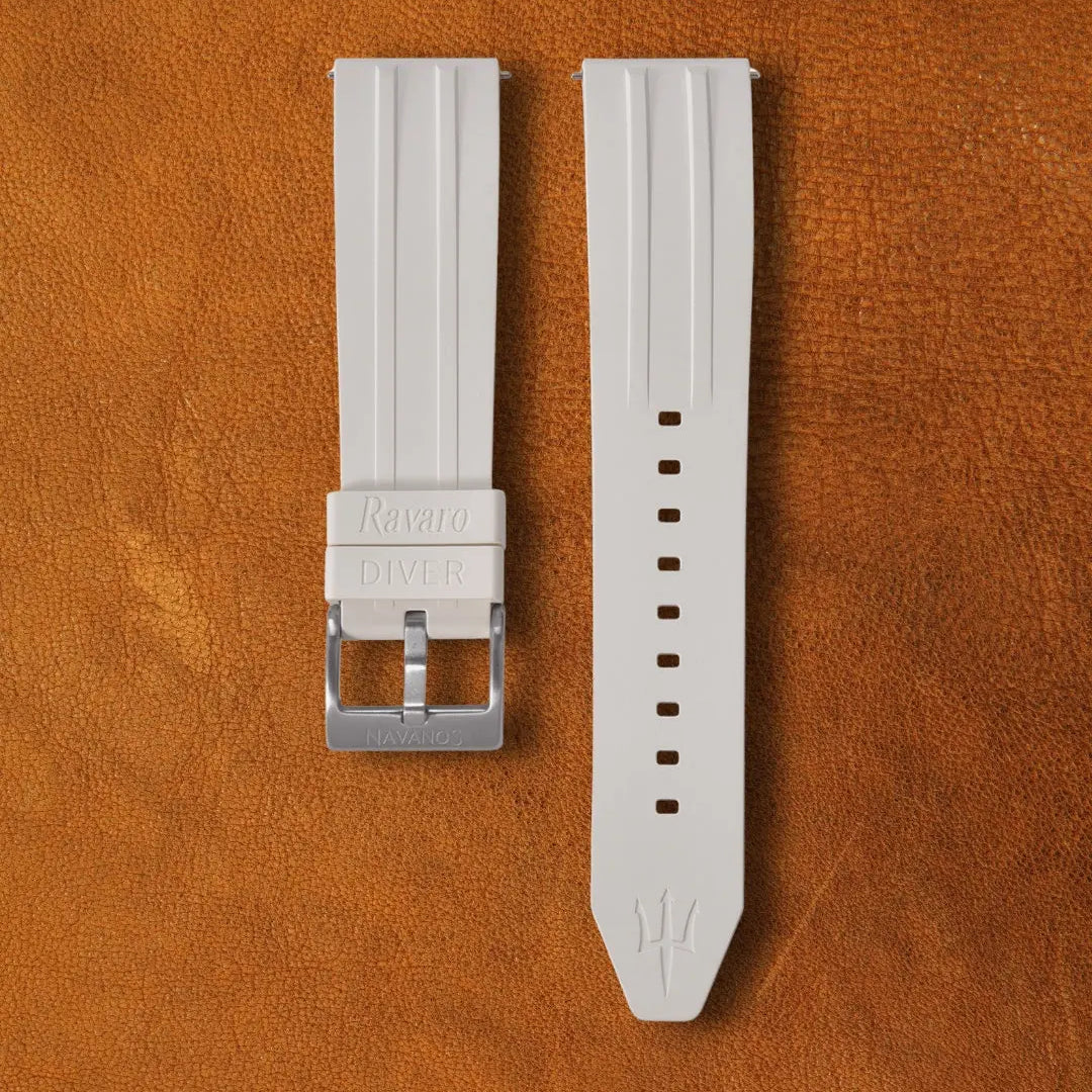Coral white Ravaro Diver FKM rubber watch strap with ribbed design, embossed "Rayaro DIVER" keeper, trident logo on tip, stainless steel tang buckle engraved "NAVANOS", quick-release spring bars, and adjustment holes, displayed on brown suede background.