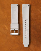 Coral white watch strap with silver buckle on a brown leather background.