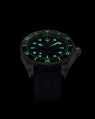 Navanos Ravaro Swiss automatic dive watch in complete darkness with powerful green Super-LumiNova lume fully illuminating the blue sunburst dial, cream markers, hands, trident logo, and bezel pip, paired with navy blue FKM rubber strap, 300m water resistance, COSC-certified Soprod P024 movement, angled studio lume shot on black background.