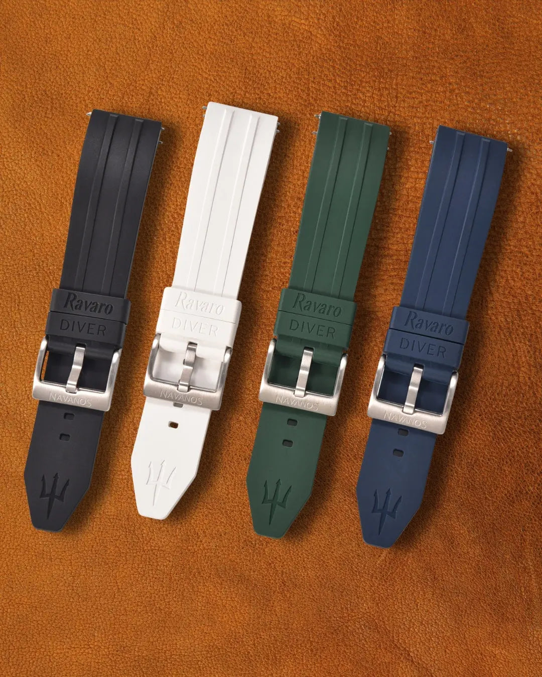Navanos Ravaro Diver rubber watch straps in onyx black, coral white, piton green, and nautica blue with embossed branding, trident logo on tip, stainless steel tang buckles, and quick-release spring bars, displayed on brown suede background.