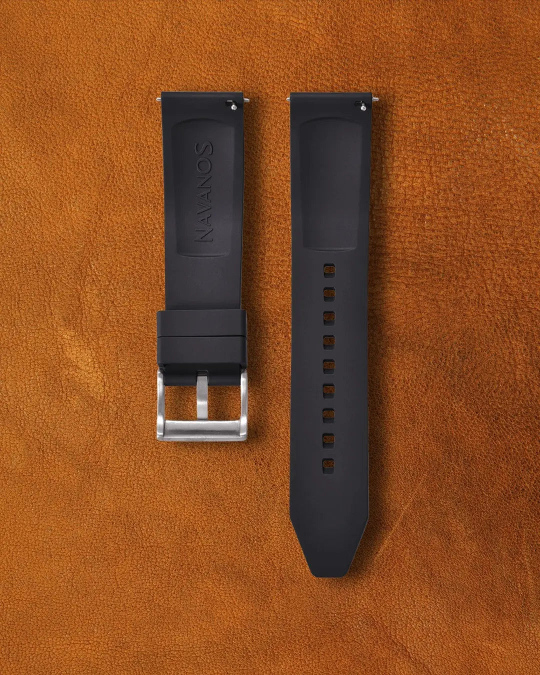 Black watch strap with silver buckle on a brown leather background.
