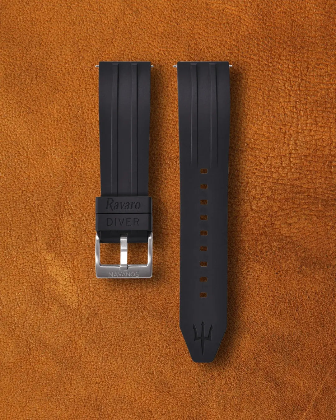 Black onyx Ravaro Diver FKM rubber watch strap with ribbed design, embossed "Ravaro DIVER" keeper, trident logo on tip, stainless steel tang buckle engraved "NAVANOS", quick-release spring bars, and adjustment holes, displayed on brown suede background.