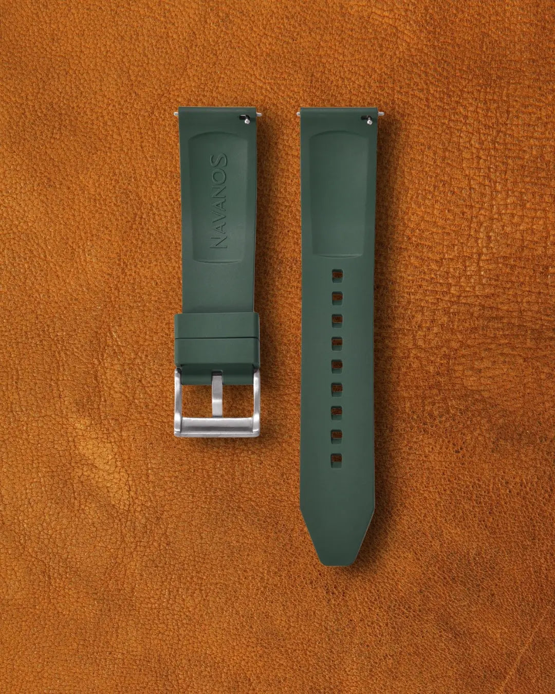 Piton green Navanos FKM rubber watch strap with embossed "NAVANOS" branding, stainless steel tang buckle, quick-release spring bars, and multiple adjustment holes, displayed on brown suede background.