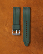 Piton green Ravaro Diver FKM rubber watch strap with ribbed design, embossed "Ravaro DIVER" keeper, trident logo on tip, stainless steel tang buckle engraved "NAVANOS", quick-release spring bars, and adjustment holes, displayed on brown suede background.