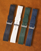 Collection of four Ravaro Diver FKM rubber watch straps in black, white, green, and blue featuring ribbed texture, embossed "Ravaro DIVER" branding, trident logo on the tip, stainless steel tang buckles engraved "NAVANOS", and quick-release spring bars, arranged on brown suede background.